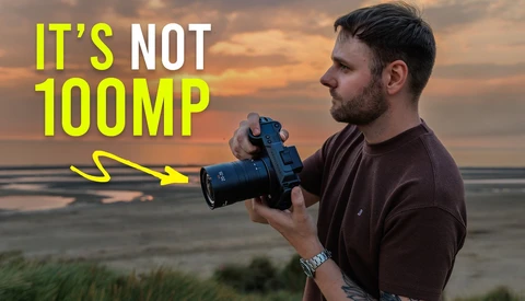 Photographer holding a mirrorless camera with telephoto lens against coastal sunset backdrop