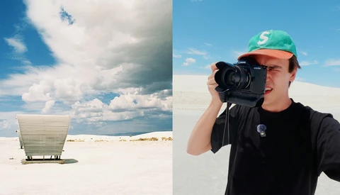 Photographer holding camera in desert landscape beside minimalist white structure
