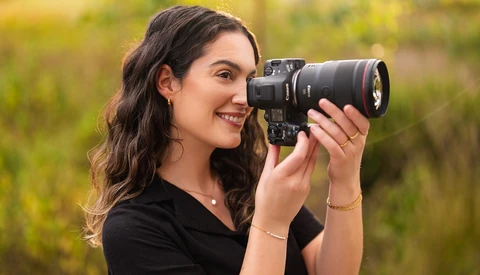 Female photographer holding a DSLR camera with telephoto lens, smiling while composing a shot outdoors