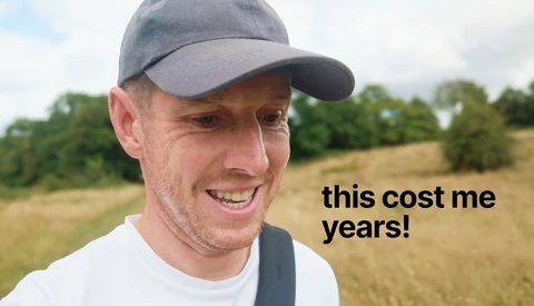 Man in baseball cap smiling at camera with rural field and trees in background