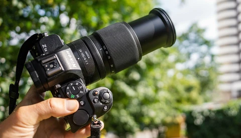 Hand holding a DSLR camera with telephoto lens outdoors in daylight