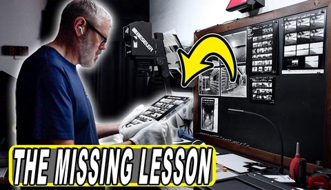 Photographer reviewing contact sheets and negatives at a light table in a darkroom setup