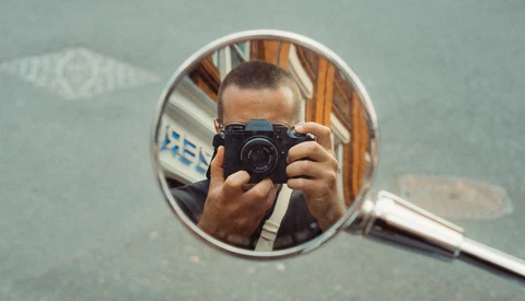 Photographer holding compact camera reflected in round mirror during self-portrait