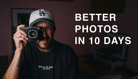 Photographer holding vintage film camera wearing LA Dodgers cap against dark interior backdrop