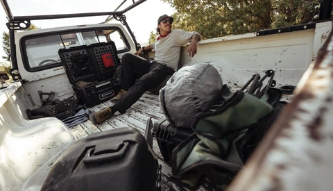 Man sitting in open truck bed with equipment and gear visible during daytime shoot