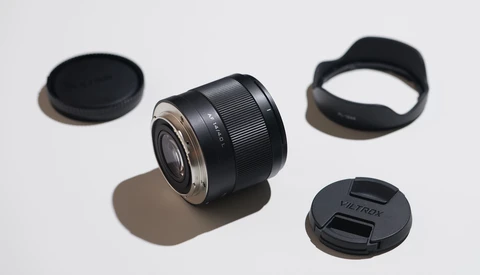 Black prime lens with lens cap, rear cap, and lens hood arranged on white surface