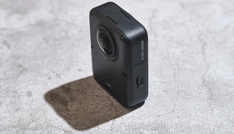 Black compact action camera with lens and side control button on concrete surface