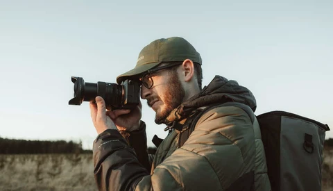 Photographer in tactical gear holding a telephoto lens camera to his face
