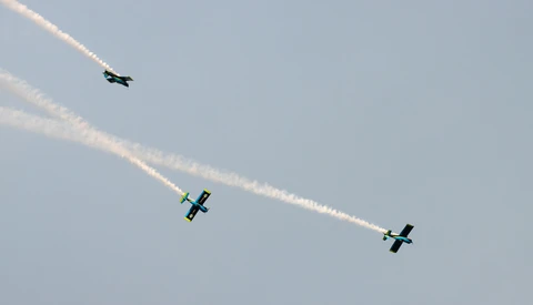 Three aerobatic aircraft in formation flight with smoke trails against a clear sky