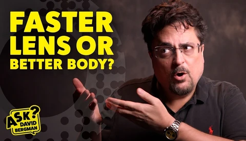 Man with glasses and beard gesturing while discussing camera equipment choice