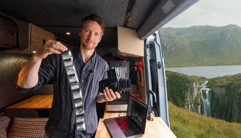 Photographer holding camera in van interior with mountain lake landscape visible through open door