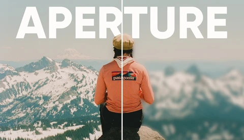 Person in orange Patagonia jacket standing on mountain ridge overlooking snowy peaks