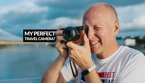 Photographer holding mirrorless camera to eye with water landscape and sky behind