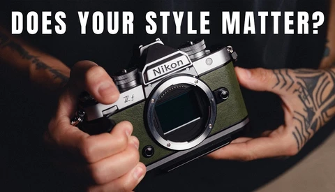 Person holding a vintage Nikon FM2 film camera with olive-green leather body and visible tattoos on their hands and arms