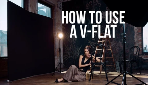 Studio portrait setup with woman seated on ladder beside professional lighting equipment and black v-flat reflector