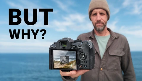 Man holding mirrorless camera displaying landscape scene on rear LCD screen