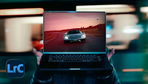 Hands holding laptop displaying sports car at sunset with LrC logo visible