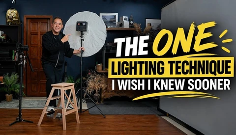 Photographer holding a large white reflector in a studio with studio lighting setup and wooden stool