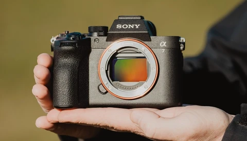 Sony Alpha mirrorless camera held in hands against yellow background, sensor visible