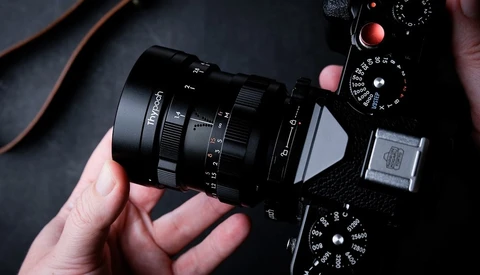 Hands holding a vintage rangefinder camera with attached lens, viewed from above