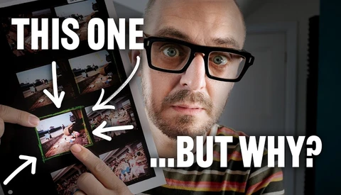 Man with glasses holding multiple printed photographs, pointing at one with a questioning expression