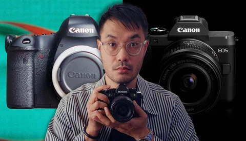 Male photographer holding a Nikon compact camera with Canon DSLRs displayed behind him