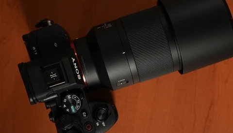 Top-down view of a Sony mirrorless camera with a long Sony lens and large lens hood resting on a reddish-brown wooden table