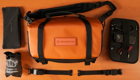 Orange Wandrd camera bag with black straps displayed flat with accessories on orange background