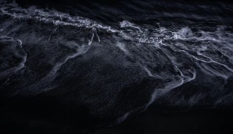 Aerial view of dark ocean water with white wave patterns and foam trails