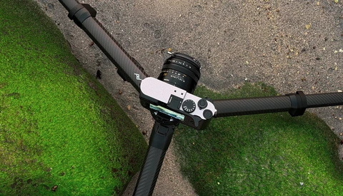 Overhead view of a mirrorless camera mounted on handlebars with moss-covered pavement