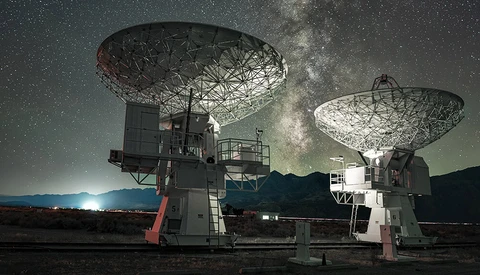 Two large radio telescope dishes pointing skyward beneath the Milky Way at night