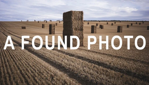 Hay bales scattered across a harvested grain field under a cloudy sky