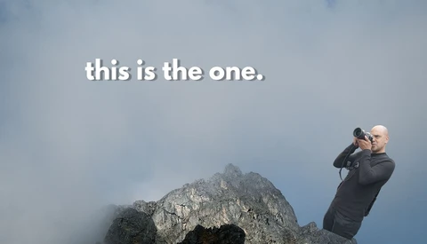 Photographer with telephoto lens photographing a dramatic rocky mountain peak shrouded in mist