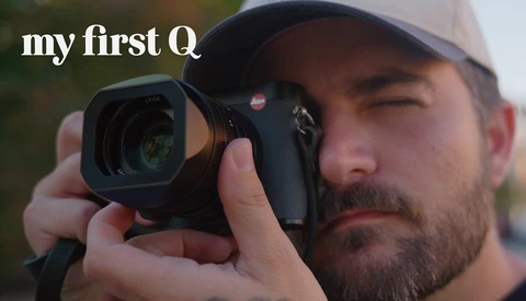 Photographer holding Leica rangefinder camera up to eye while wearing cap