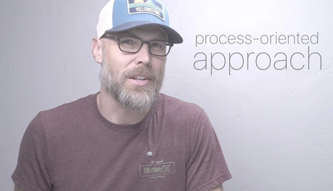 Man wearing glasses and cap speaking, with 'process-oriented approach' text overlay