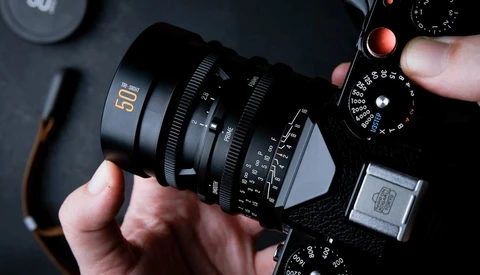 Hands holding a cinema camera lens with focal length markings visible on dark background