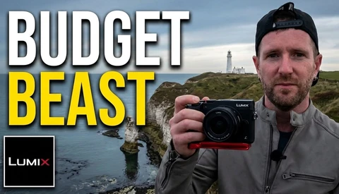 Man holding Lumix camera against coastal cliff landscape with lighthouse