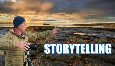 Photographer with camera on tripod gesturing toward coastal landscape at golden hour with lighthouse in distance