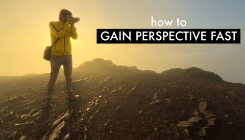 Photographer in yellow jacket standing on rocky terrain at sunrise with mountains in background