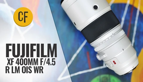 Fujifilm XF 400mm F/4.5 R LM OIS WR telephoto lens with white barrel and black grip ring, shown on a colorful abstract painted background