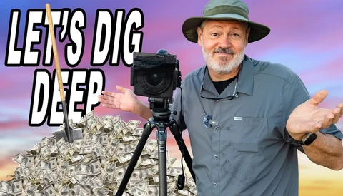 Bearded man in a bucket hat shrugs beside a tripod-mounted camera in front of a pile of cash and a shovel.