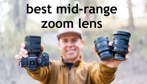 Smiling man in a white cap and tan jacket holding up a mirrorless camera with a zoom lens and two other lenses outdoors, with the text 'best mid-range zoom lens'.