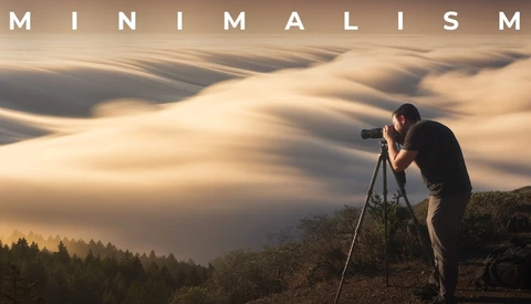 Photographer shooting from a tripod on a hilltop above wave-like fog rolling over forested hills in warm golden light