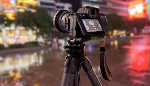Mirrorless camera with a lens mounted on a carbon fiber tripod, rear screen angled out, set on a wet city street at night.