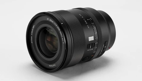 Black 35mm f/1.4 autofocus camera lens angled on a light gray studio backdrop, showing its front element and barrel markings