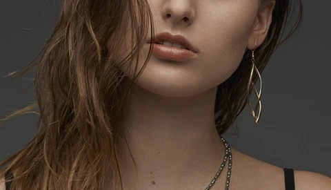 Portrait of woman with long brown hair and statement earrings against neutral gray background.