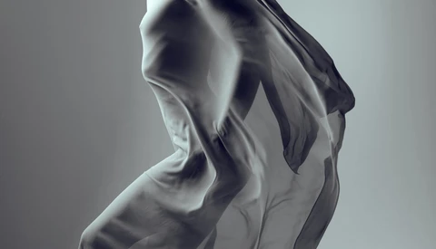 Translucent fabric draped and billowing against a neutral gray background, creating soft sculptural folds.