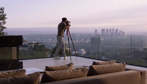 Photographer on a modern rooftop terrace with a camera on tripod, overlooking a sprawling city skyline at dusk.