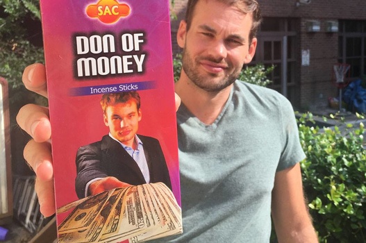 Lee Morris of Fstopper holding a leaflet with a photo of himself holding some twenty dollar bills.