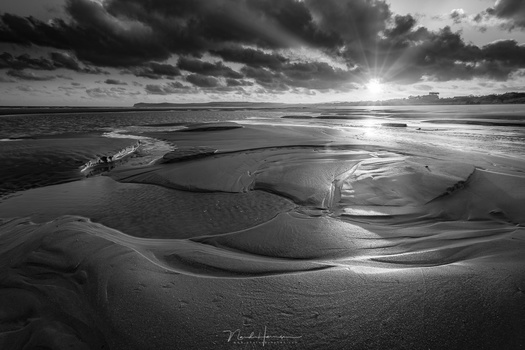 A sunrise at a beach. The sun is the brightest subject in the photo, and all attention is going to that bright spot. The patterns in the sand comes second. If black and white turns out to be very beautiful, you might consider keeping it black and white.